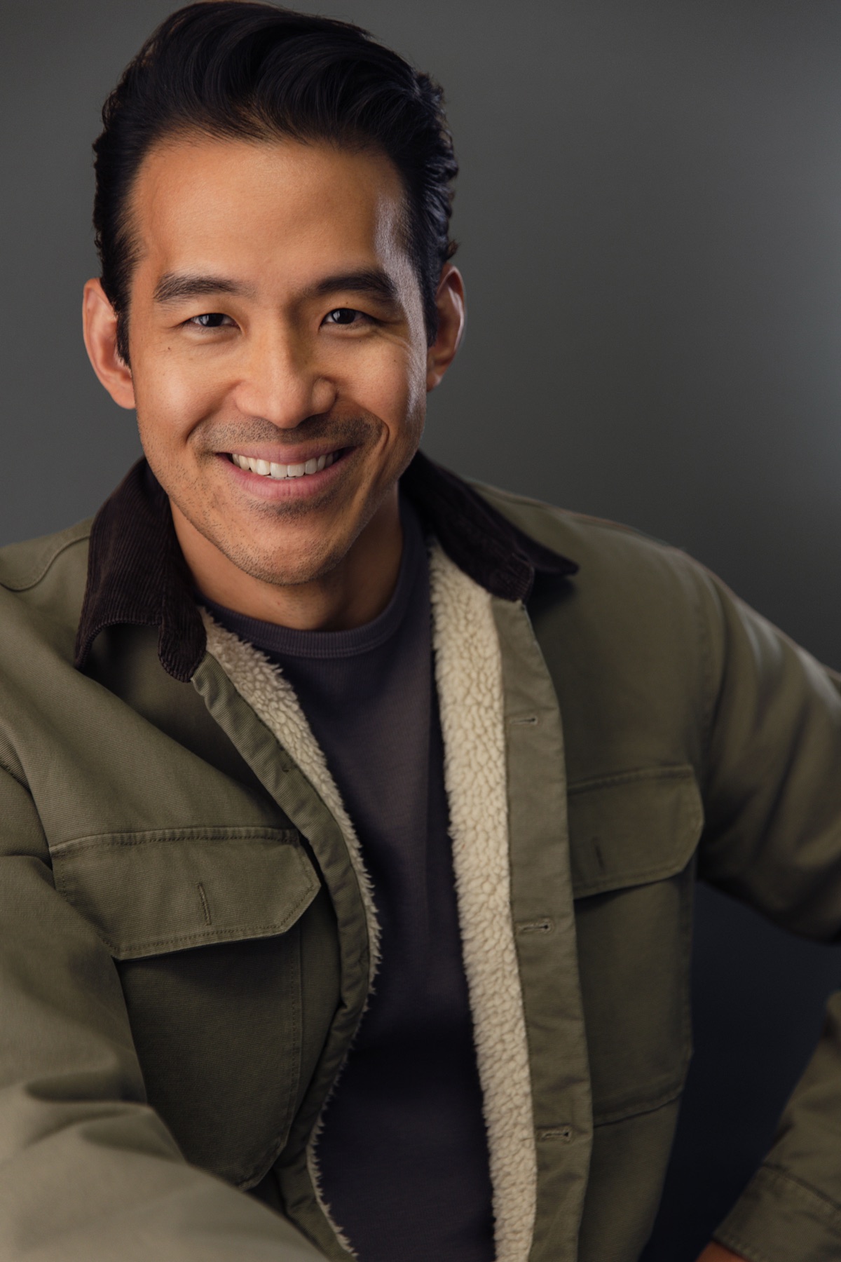 Alex Chung smiling warmly in an olive jacket with a shearling collar.